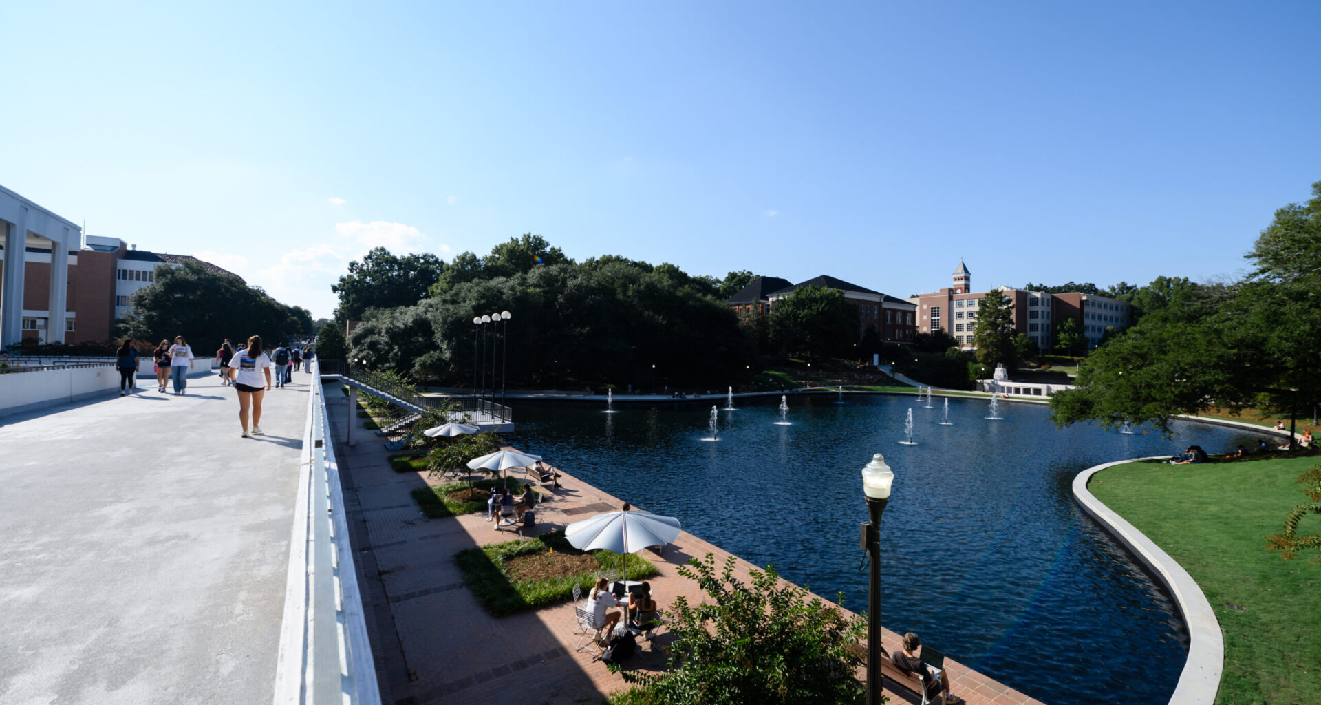 Individuals walk across a bridge next to a pond