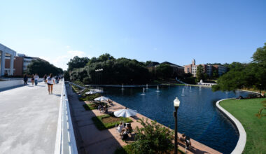 Individuals walk across a bridge next to a pond