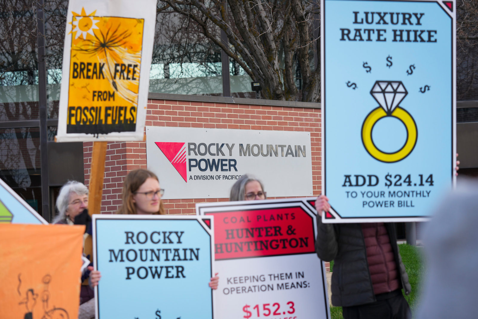 Photo of protesters holding signs, inspired by the game Monopoly, that protest their utility's rate hikes and use of fossil fuels