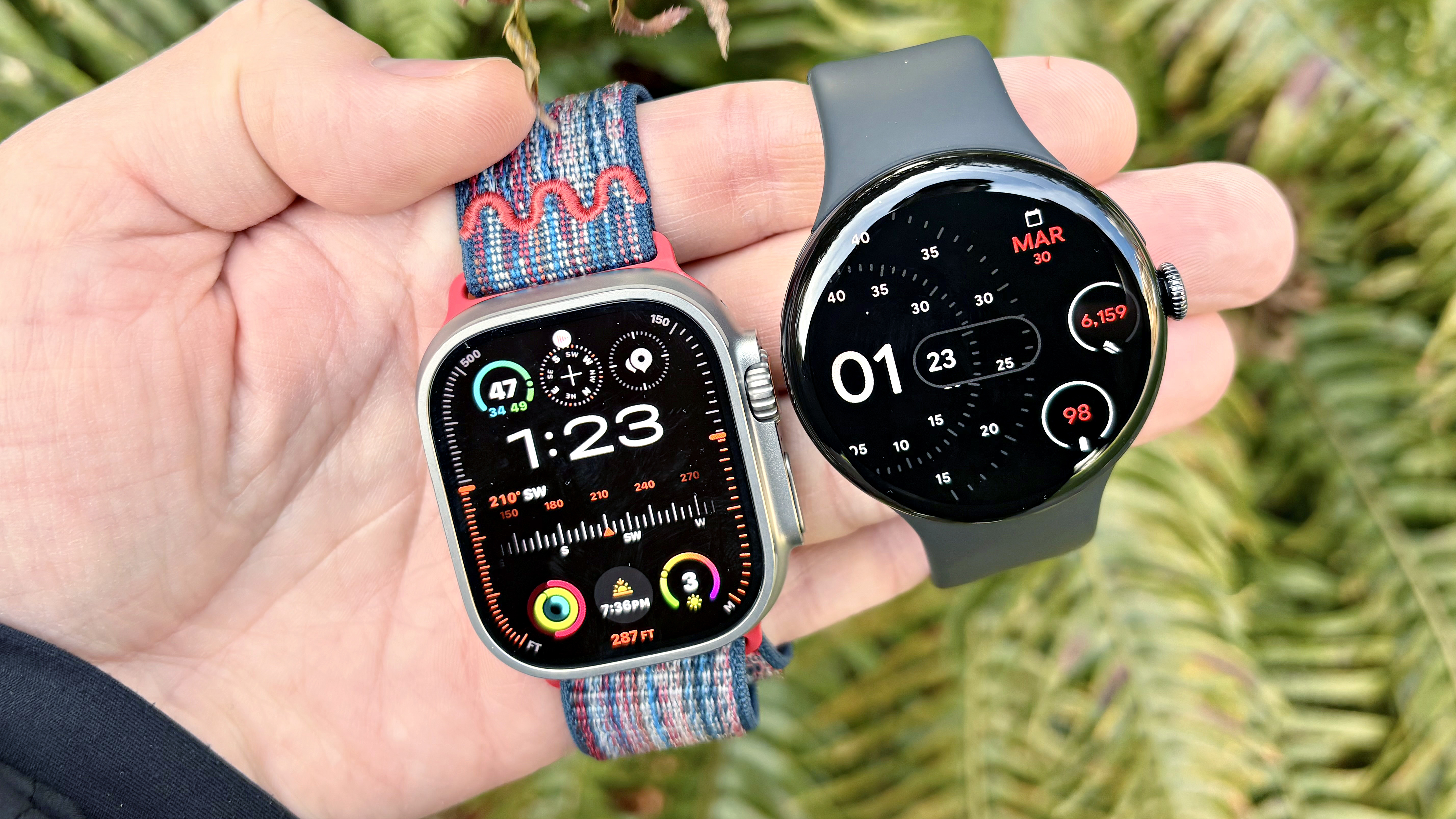 Close-up of the Apple Watch Ultra 3 and Google Pixel Watch 4 in a user's hand against a colorful out-of-focus background
