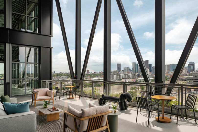 Modern outdoor terrace by Morris Adjmi Architects with seating, tables, and decorative sculptures, overlooking a city skyline through large black steel beams.