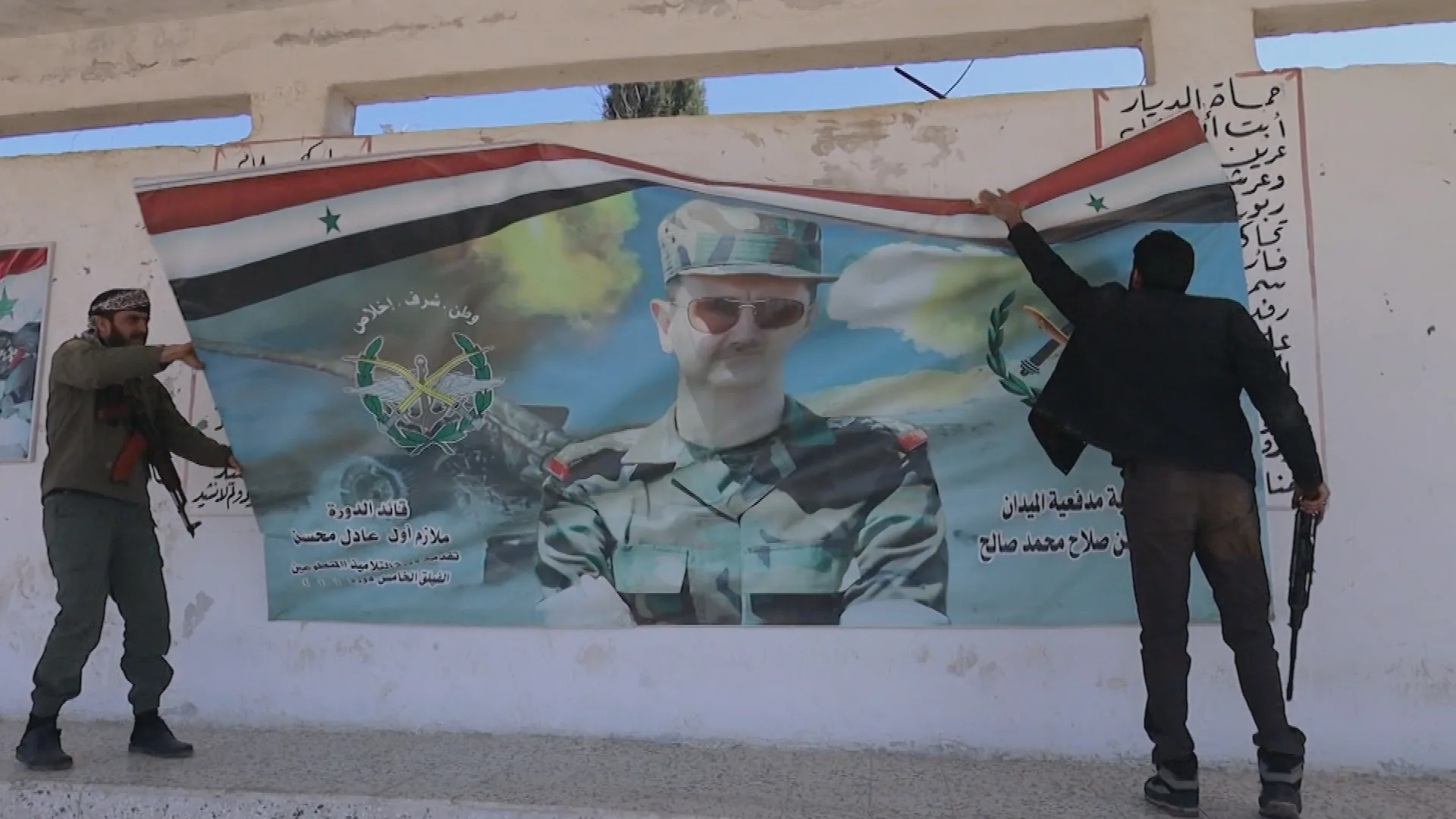 Two people carrying firearms tear down a poster of former Syrian President Bashar al-Assad.