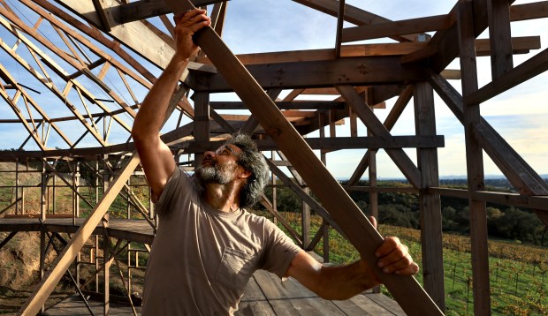 Ken Moholt-Siebert, adjusts wires used to secure rafters due to an incoming storm, on a replica of Santa Rosa's round barn, Monday, Nov. 10, 2025, on property he owns, a little over a mile north of the original round barn which burned to the ground during the 2017 Tubbs Fire. (Kent Porter / The Press Democrat)