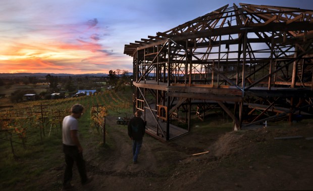 Ken Moholt-Siebert, left, and David Wycoff knock off for the day, after securing rafters due to an incoming storm. Moholt-Siebert is building, mostly without machinery, a true to size replica of Santa Rosa's round barn, Monday, Nov. 10, 2025, on property he owns, a little over a mile north of where the original round barn burned to the ground during the 2017 Tubbs Fire. (Kent Porter / The Press Democrat)