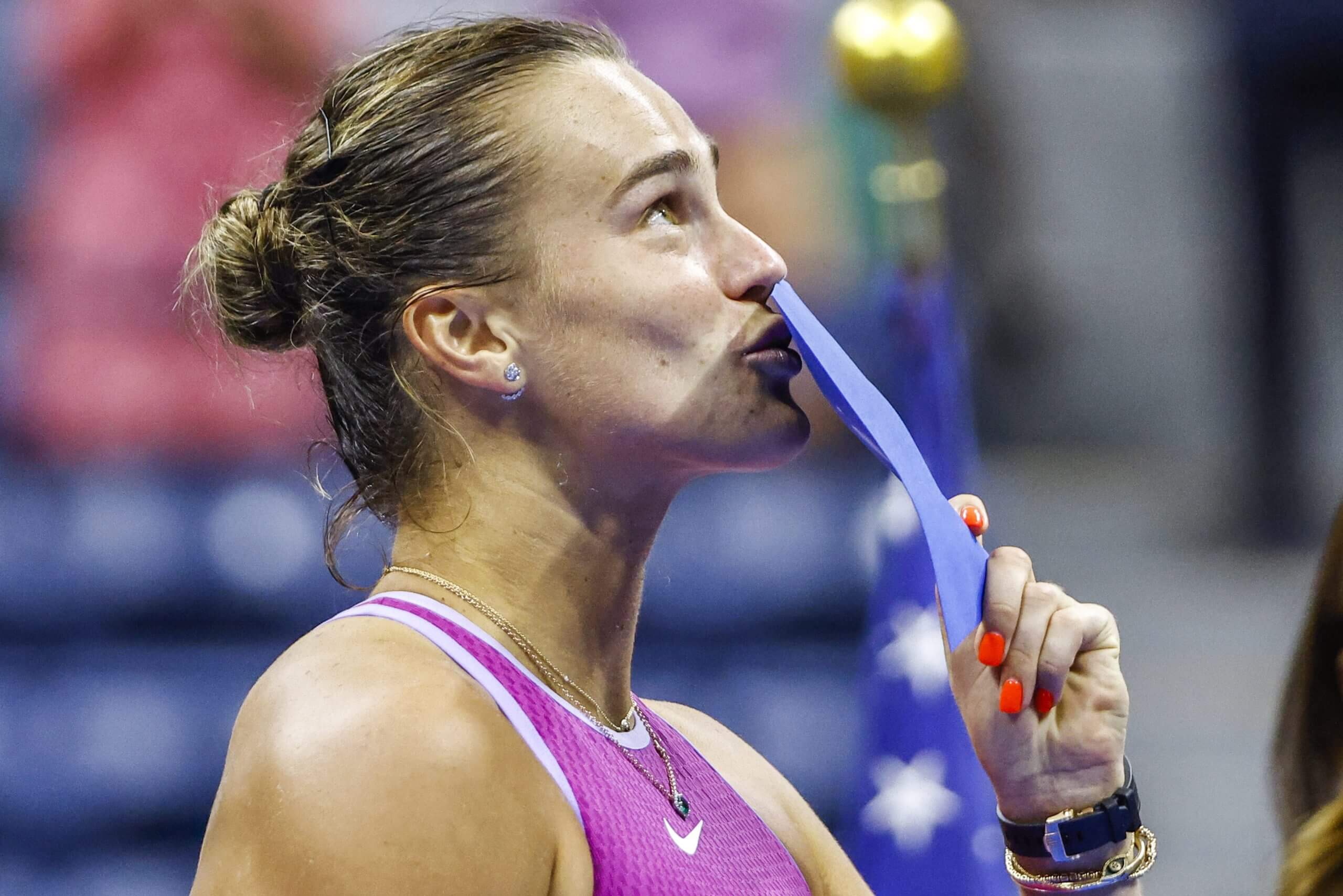 Aryna Sabalenka kisses an envelope while looking up at a trophy ceremony.