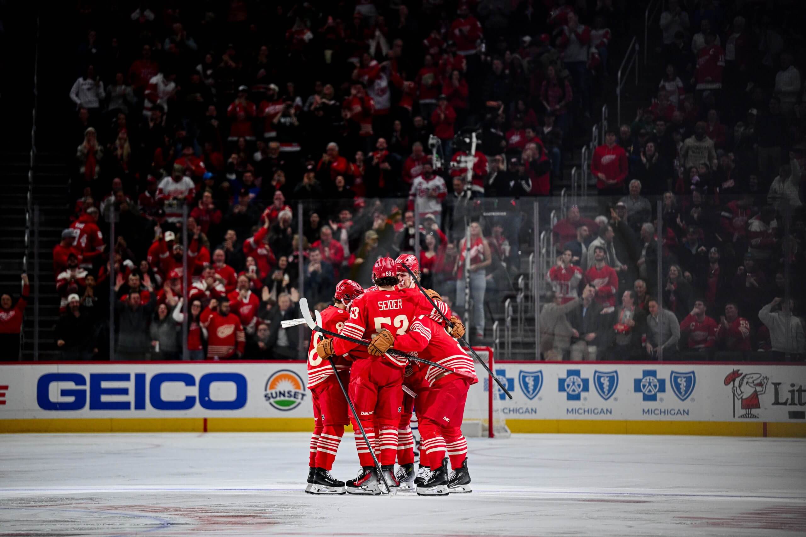 Red Wings players hug in the middle of the ice with a cheering crowd in the background.