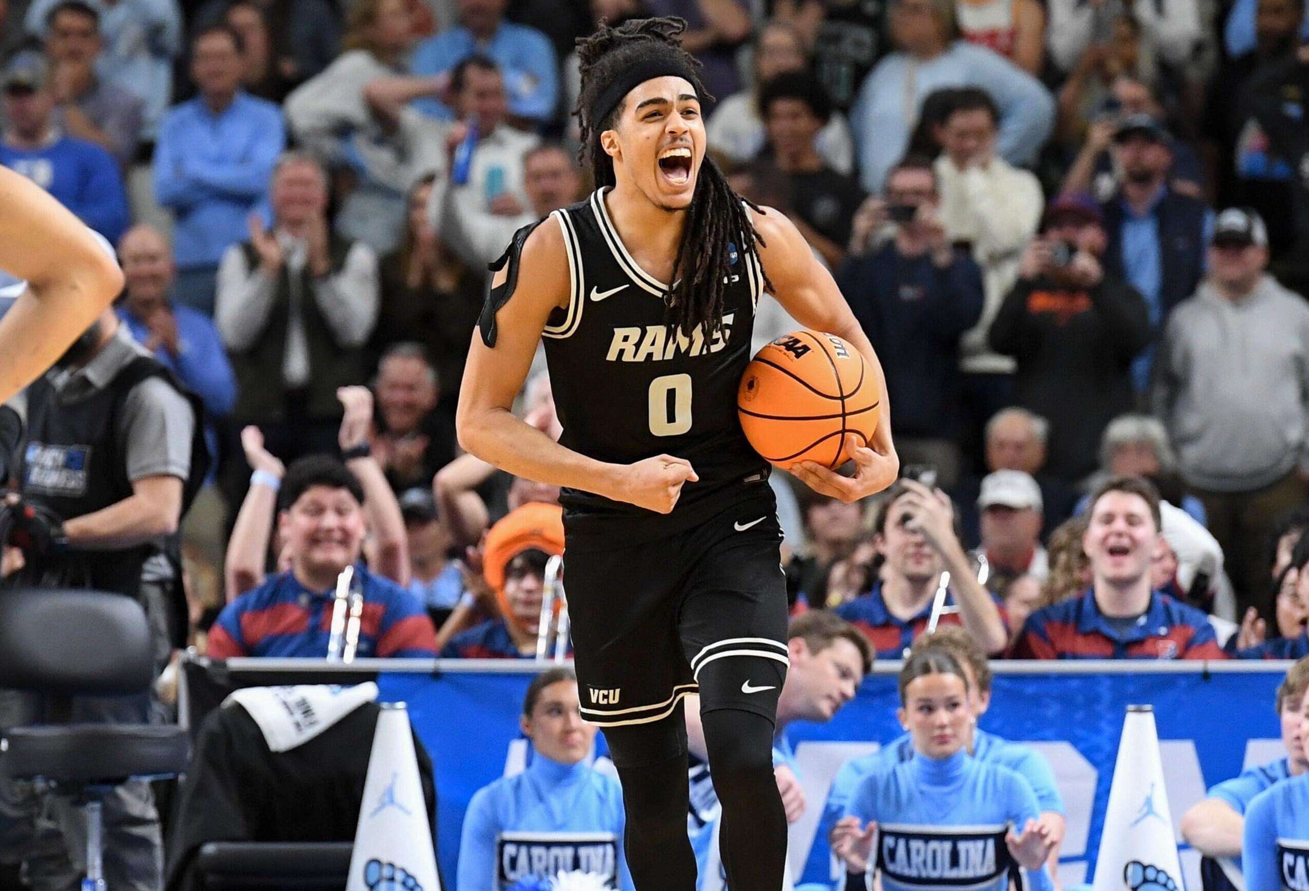 A men's basketball player yells with joy while holding the ball in his left arm.