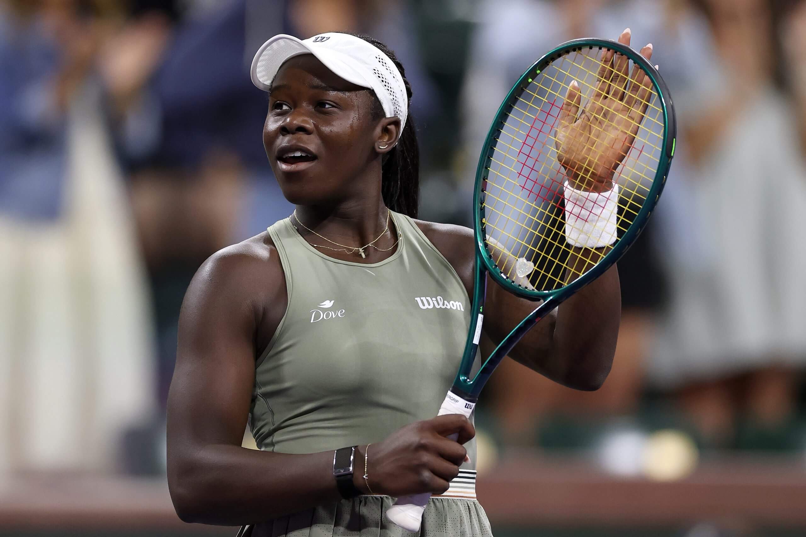 Victoria Mboko claps her racket to acknowledge the crowd at a tennis match while wearing a grey tennis outfit.