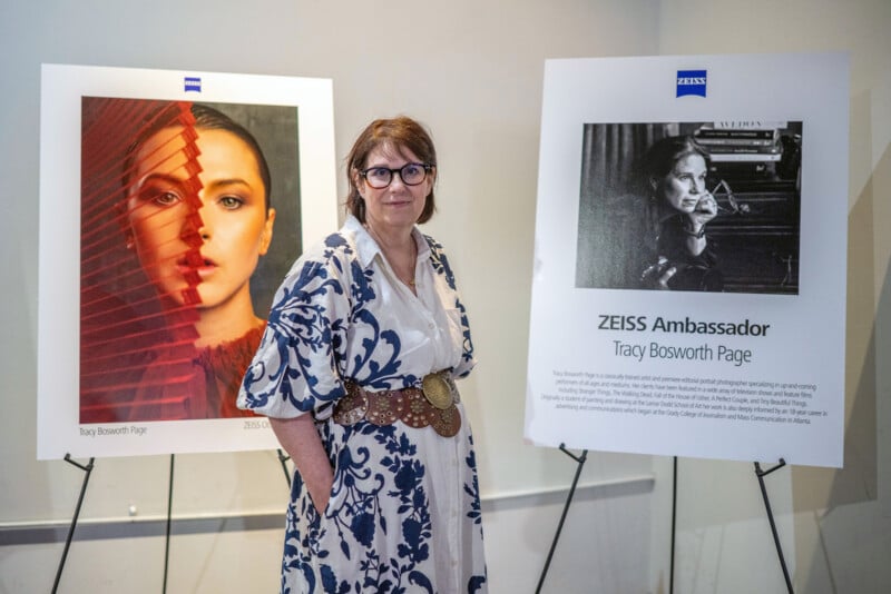 A woman in patterned dress and glasses stands between two posters—one features a portrait of a woman behind red blinds, the other introduces her as ZEISS Ambassador Tracy Bosworth Page.