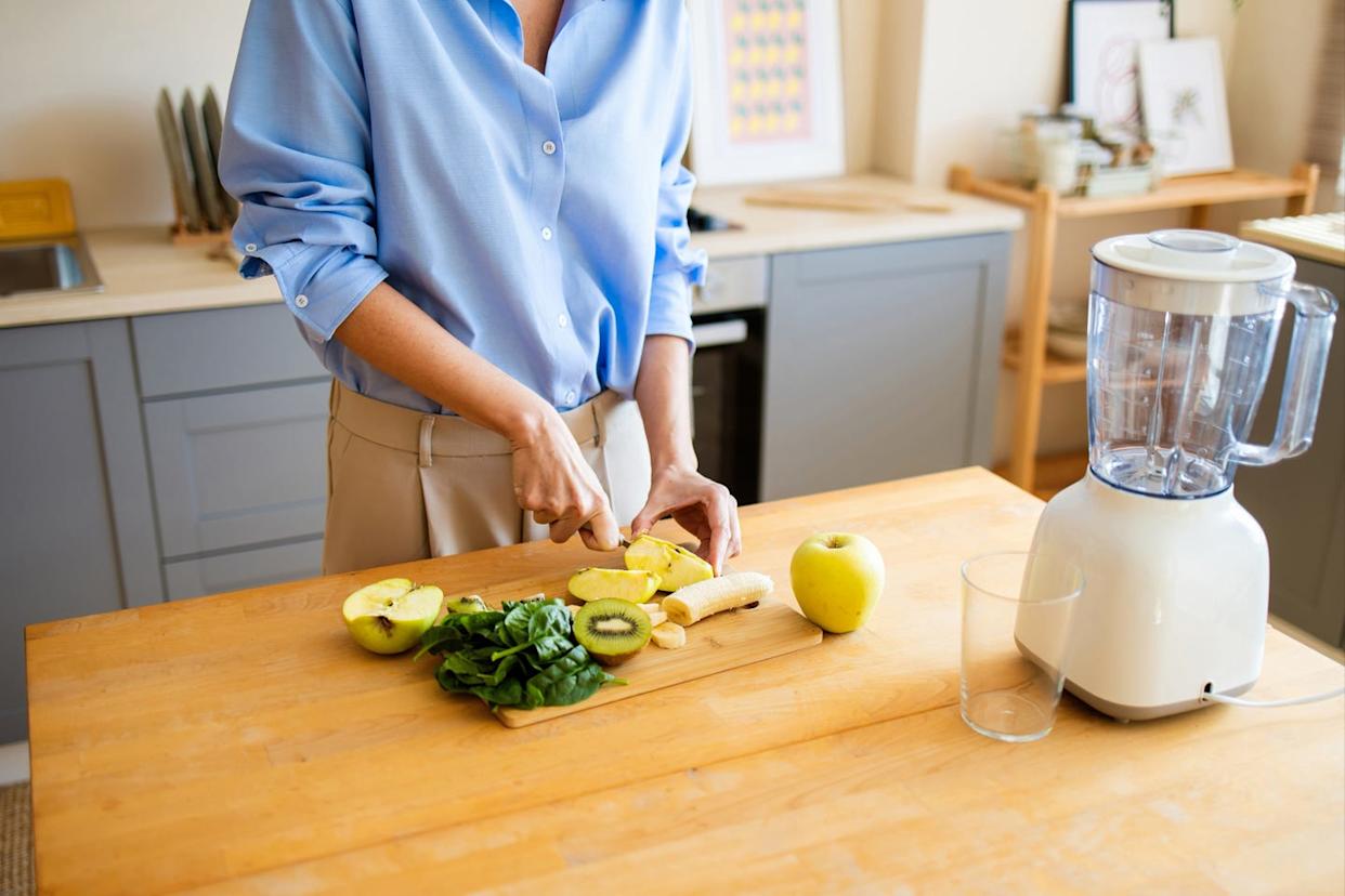 Woman preparing green fruit smoothie in kitchen