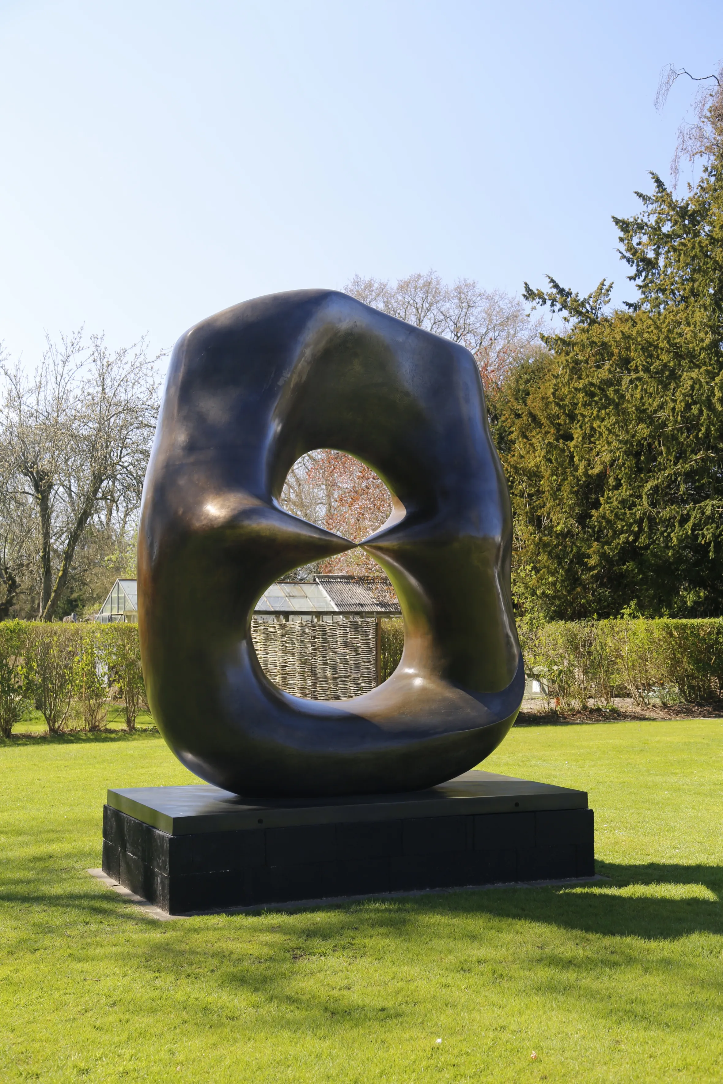 Bronze sculpture "Oval with Points" by Henry Moore, featuring an abstract, organic shape with two points almost touching within an oval opening, set on a dark plinth in a grassy garden.
