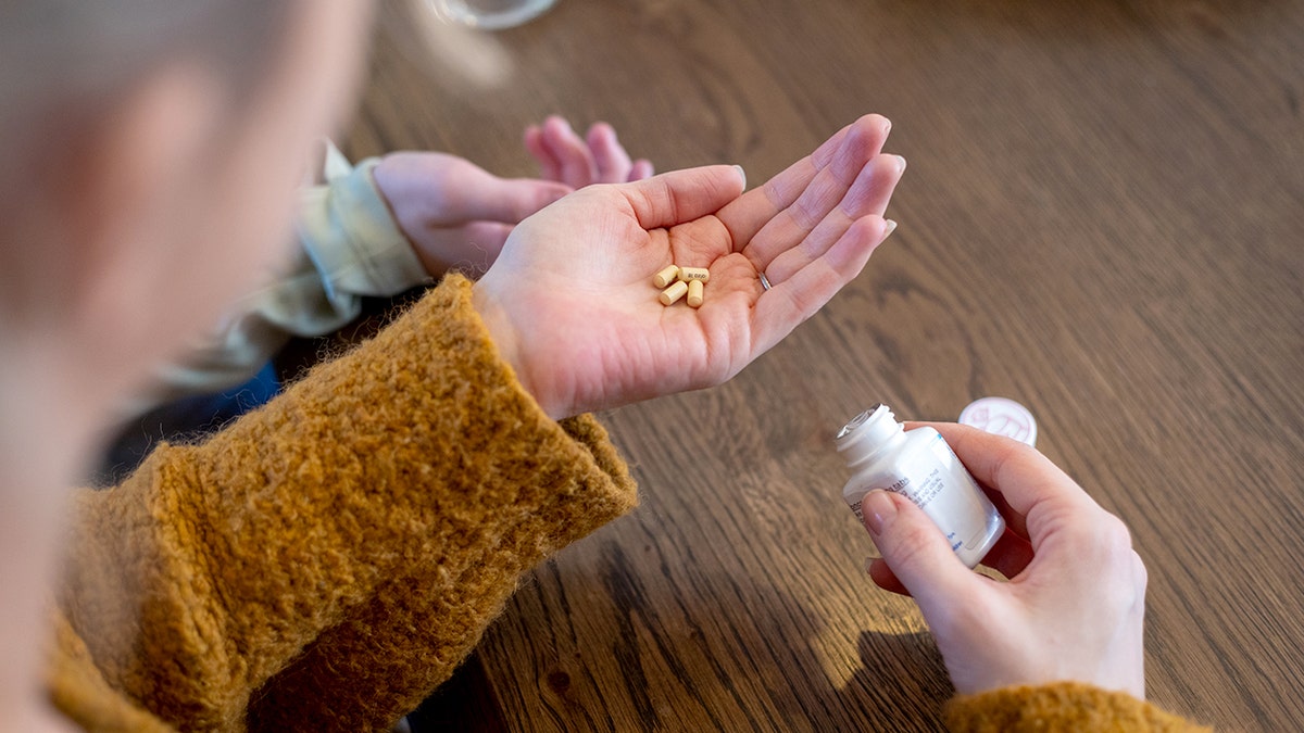 Medium close-up of a mother holding medication for her daughter, the child is reaching out towards the hand to receive the medication. They are in the kitchen of their home located in Newcastle Upon Tyne.