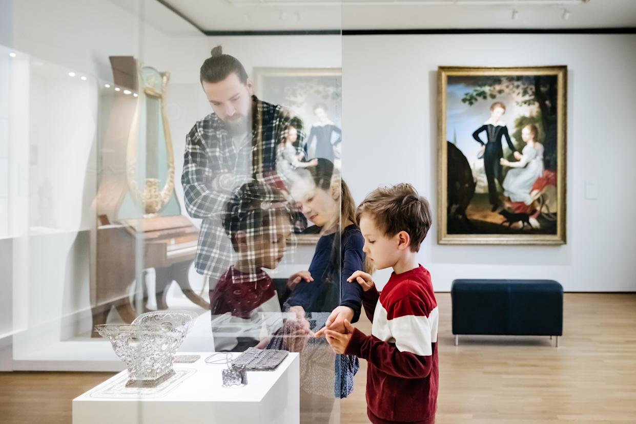 A single father looking at various objects on display in a museum while spending the day out with his two young children.