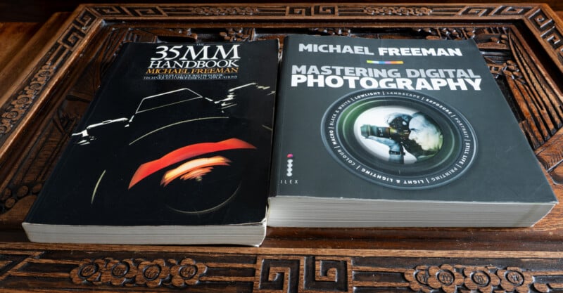 Two photography books by Michael Freeman on a carved wooden table: "35MM Handbook" with a stylized cover and "Mastering Digital Photography" featuring a photographer with a DSLR camera.