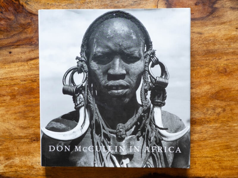 A book titled "Don McCullin in Africa" featuring a black and white photo of a person with traditional jewelry and adornments on the cover, placed on a wooden surface.