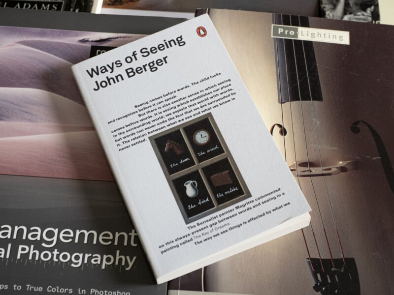 A copy of "Ways of Seeing" by John Berger rests on top of several photography books. The cover features four labeled images: a shoe, a clock, a jug, and a pair of painted rectangles.