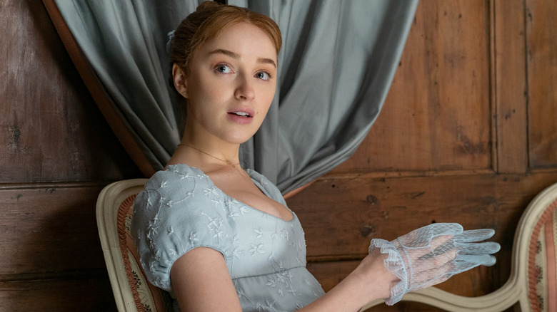 Phoebe Dynevor as Daphne in a blue dress putting lace gloves on in Bridgerton