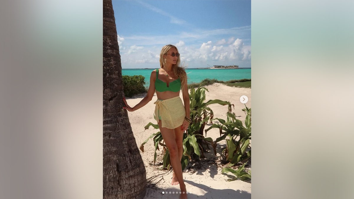 Brittany Aldean posed in a green bikini while leaning on a palm tree.