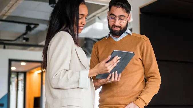 Shot of two business professionals standing in an office and reviewing some financial data on an electronic tablet