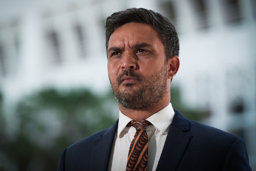 A man wearing a suit and tie has a serious facial expression.