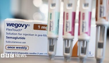 Close up of a counter top with a white box of Wegovy weight loss drug behind four out of focus pens used to inject the drug