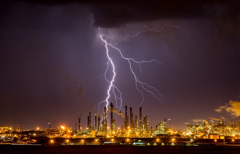 Lightning strike in a night sky over a built-up area glowing with lights.