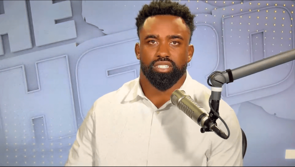 Man with beard and white shirt speaking into a microphone.