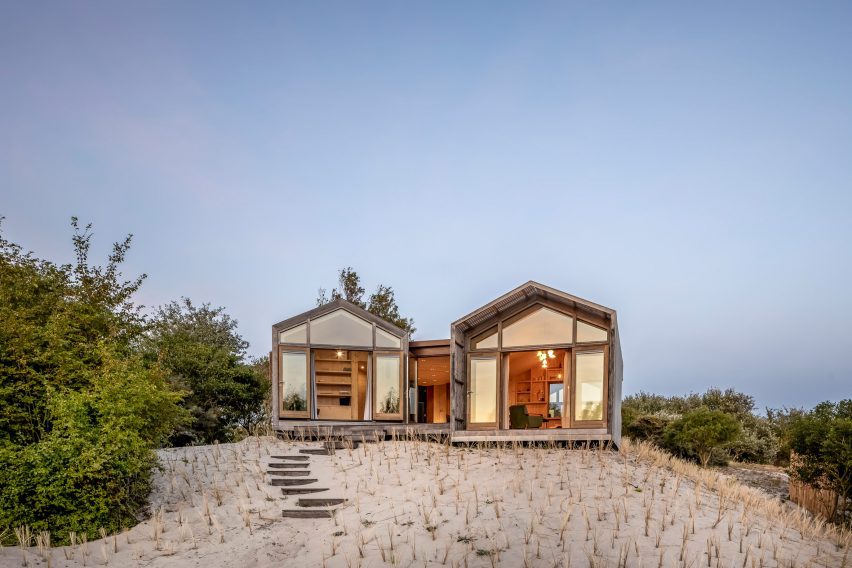 A glass and wood house on top of a sandy beach.