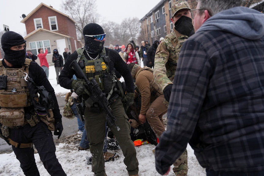 A man faces a group of federal agents with their faces covered