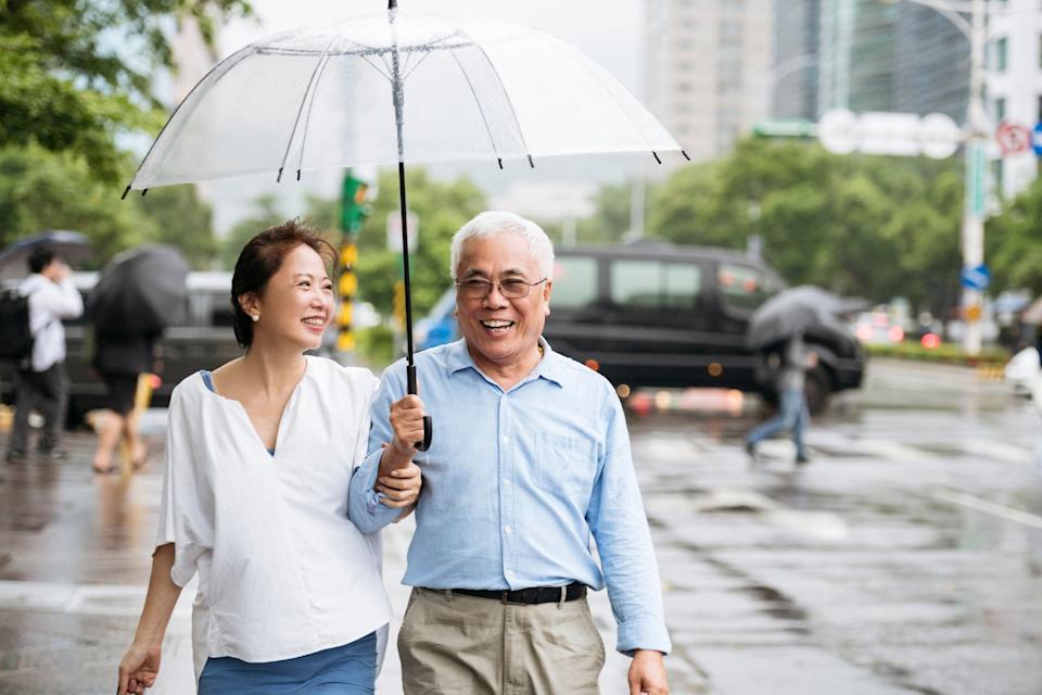 A retired couple holds an umbrella while walking on a rainy day.