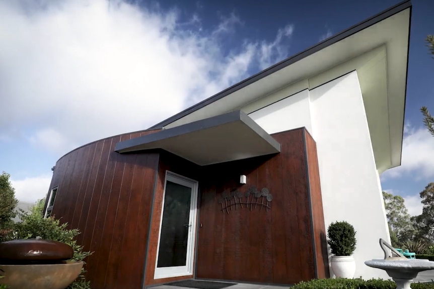 A house with a round section in brown and a square section in white with a veranda.