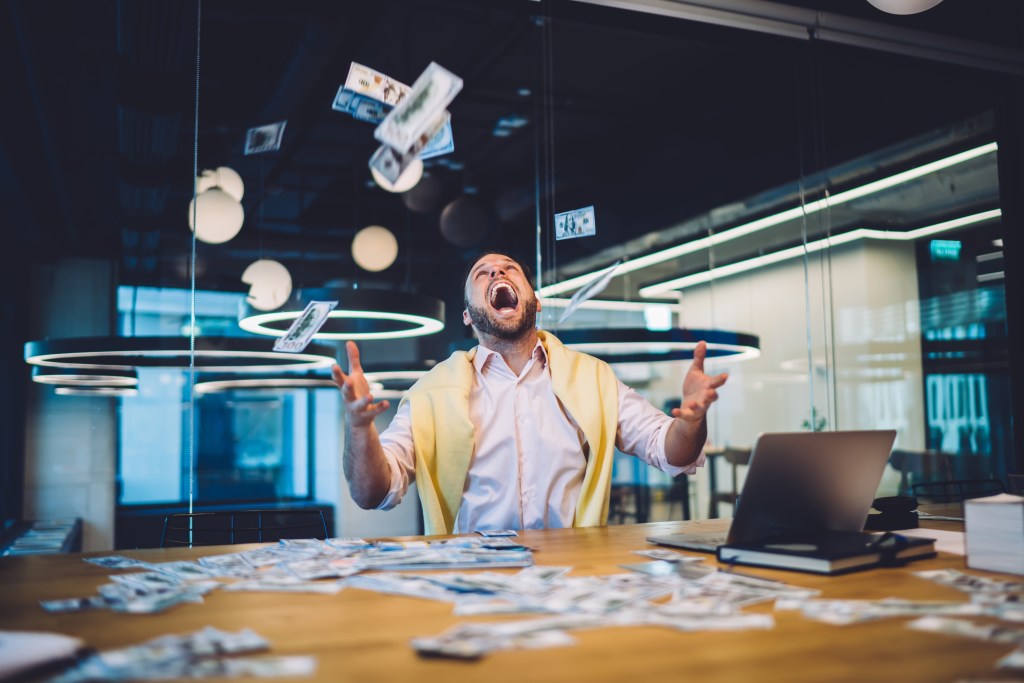 An excited man with money falling around him.