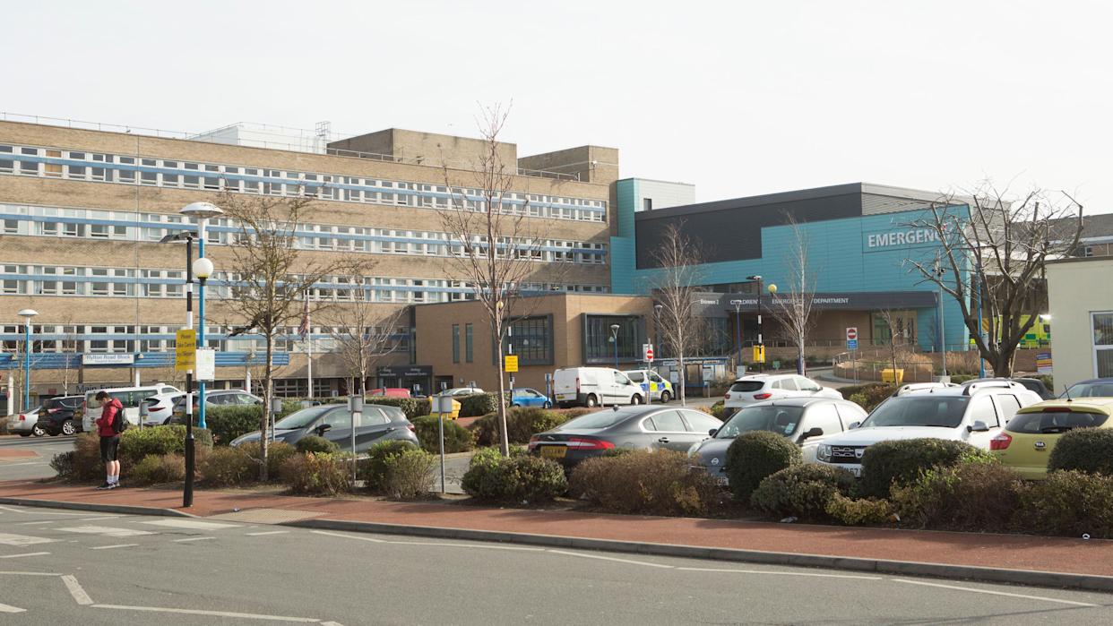 Sunderland Royal Hospital is a five-storey brick building with rows of windows. A section of the building, which is blue, juts out. There is also a car park out front.