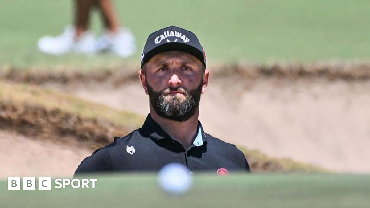 Jon Rahm playing from a bunker. His ball is in the foreground of the image.