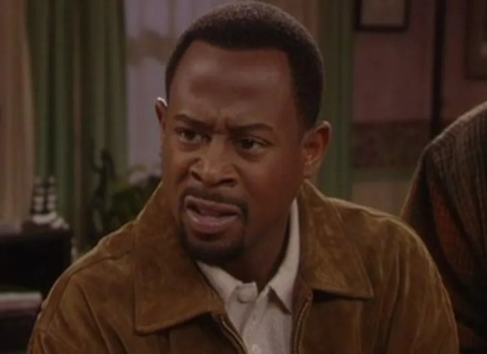 Person in an indoor setting with a puzzled expression, wearing a suede jacket over a collared shirt