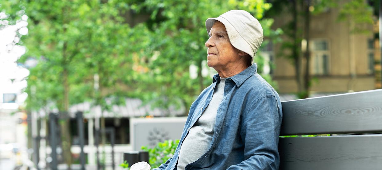 An older man drinking coffee on a bench outside.