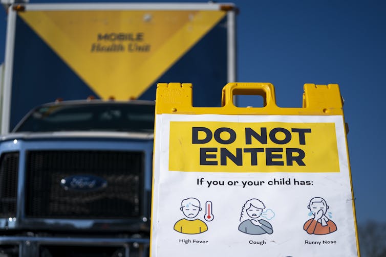 A sign in front of a mobile health vehicle asks people not to enter if they are experiencing measles symptoms.