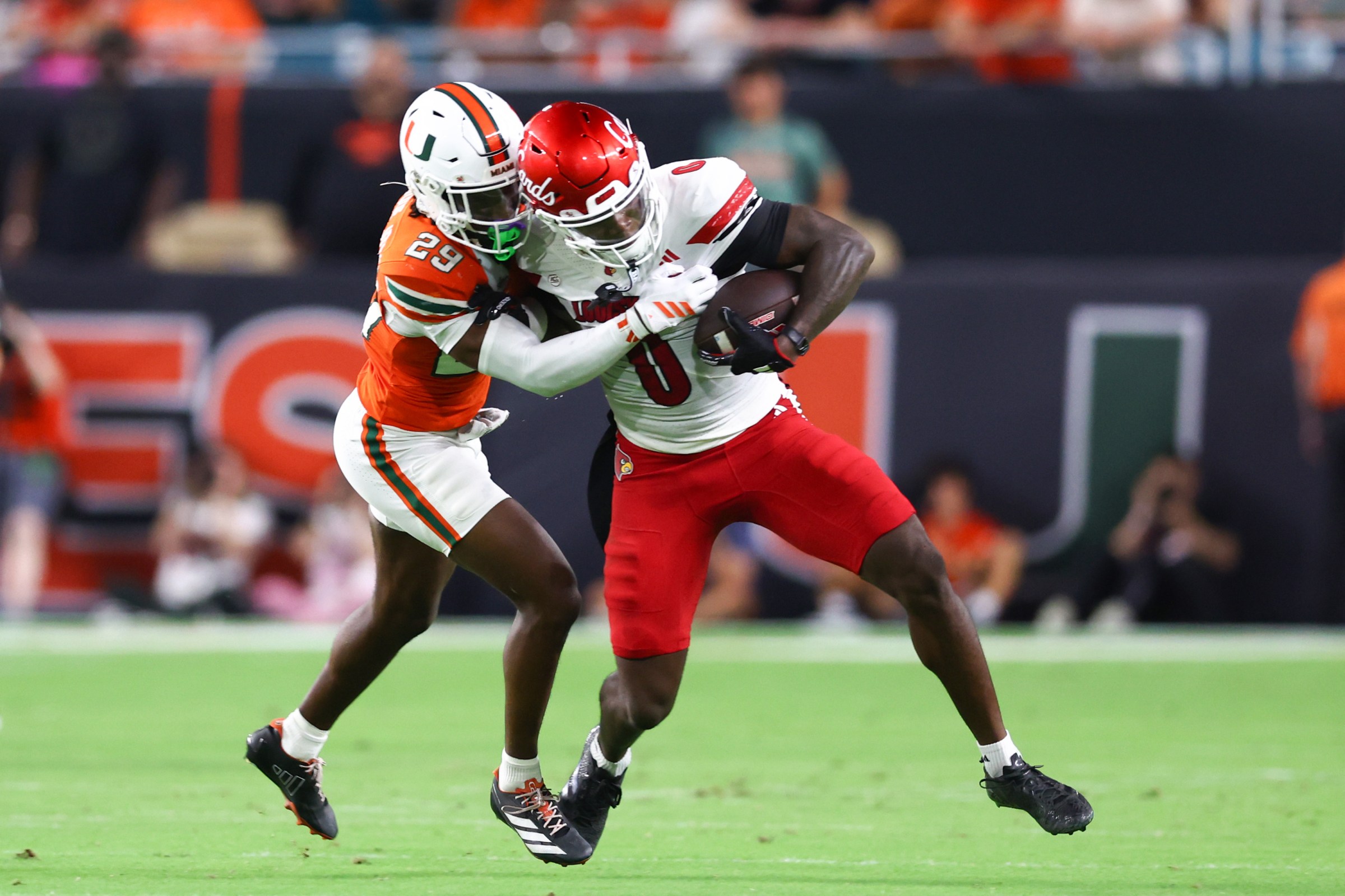 MIAMI GARDENS, FLORIDA - OCTOBER 17: Chris Bell #0 of the Louisville Cardinals carries the ball against Jr. Romanas Frederique #29 of the Miami Hurricanes during the first half of the game at Hard Rock Stadium on October 17, 2025 in Miami Gardens, Florida. (Photo by Megan Briggs/Getty Images)
