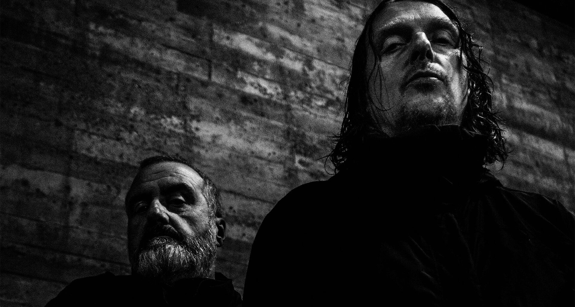 Studio promotional photo of Godflesh featuring members Justin Broadrick and G. C. Green posed against a dark industrial backdrop.