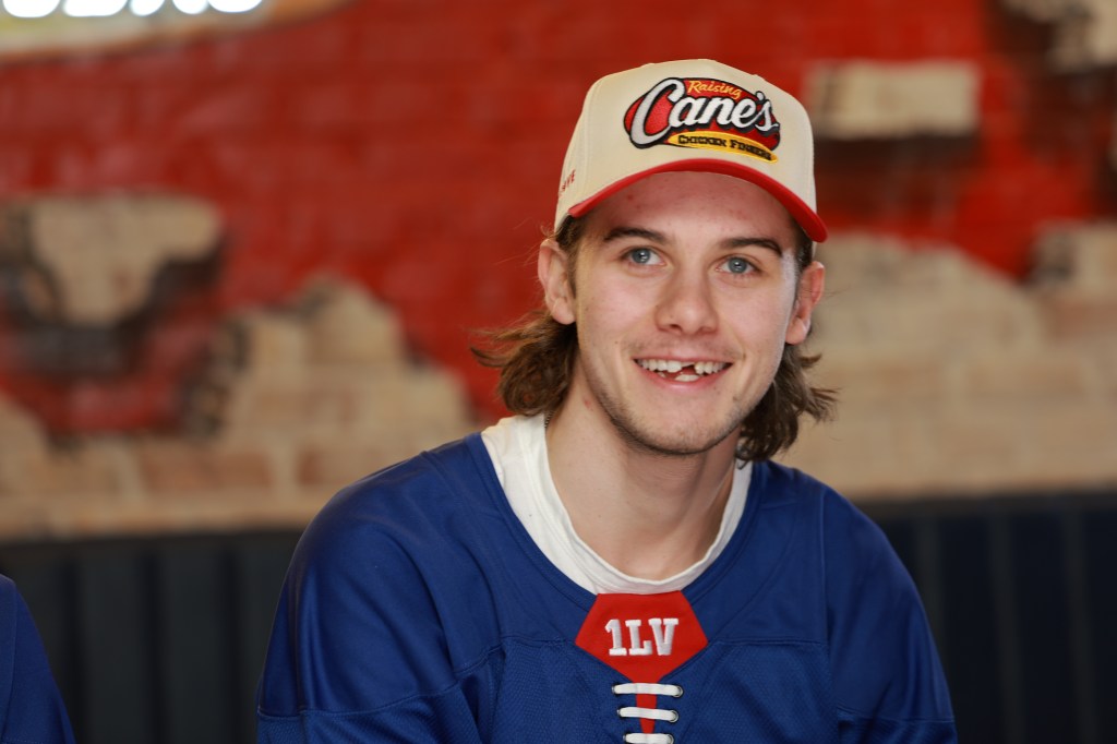 Jack Hughes in a blue jersey and a Raising Cane's hat, smiling.