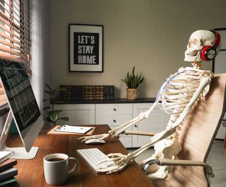 Human skeleton sat at a computer desk with headphones on.