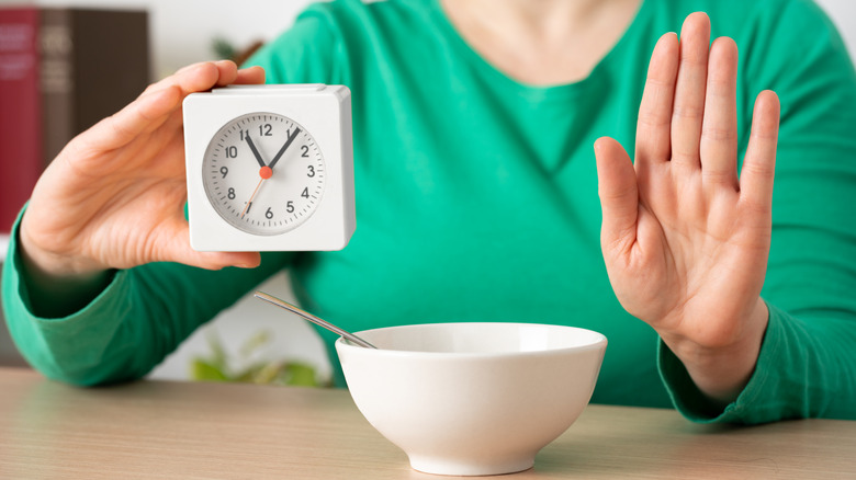 Person's hand up in front of white bowl with a clock in the other hand