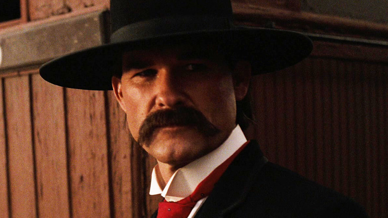 Kurt Russell's Wyatt Earp stands against a wooden wall in Tombstone