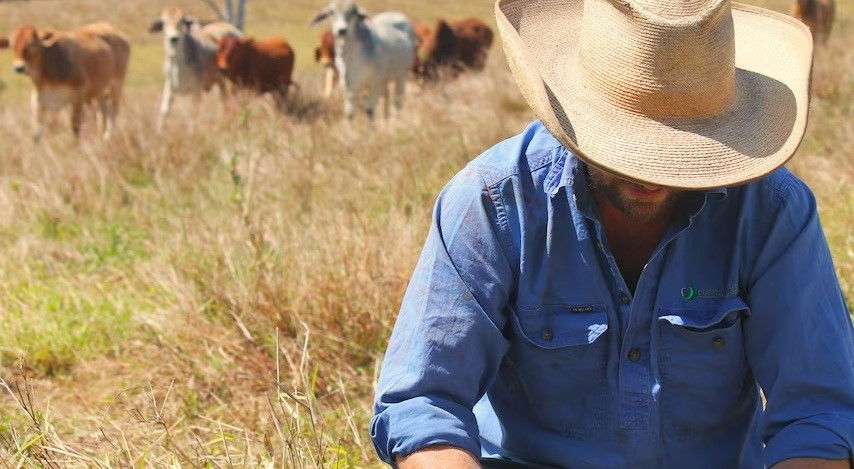 A farmer covered by a hate with goats in the background