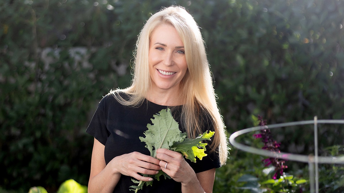 Lee Cotton smiles as she holds home-grown vegetables in a garden.