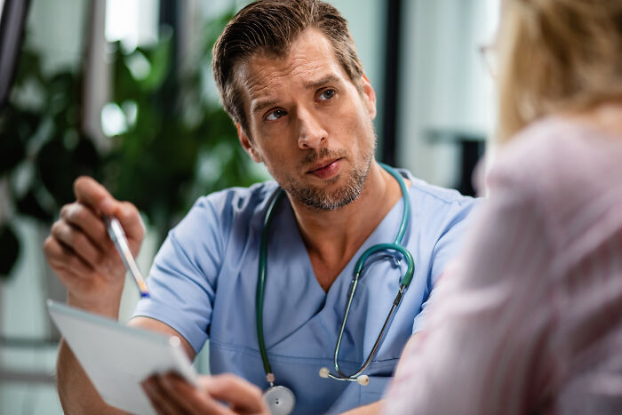 Doctor in blue scrubs with stethoscope discussing feelings and opinions with a patient in a medical office setting.