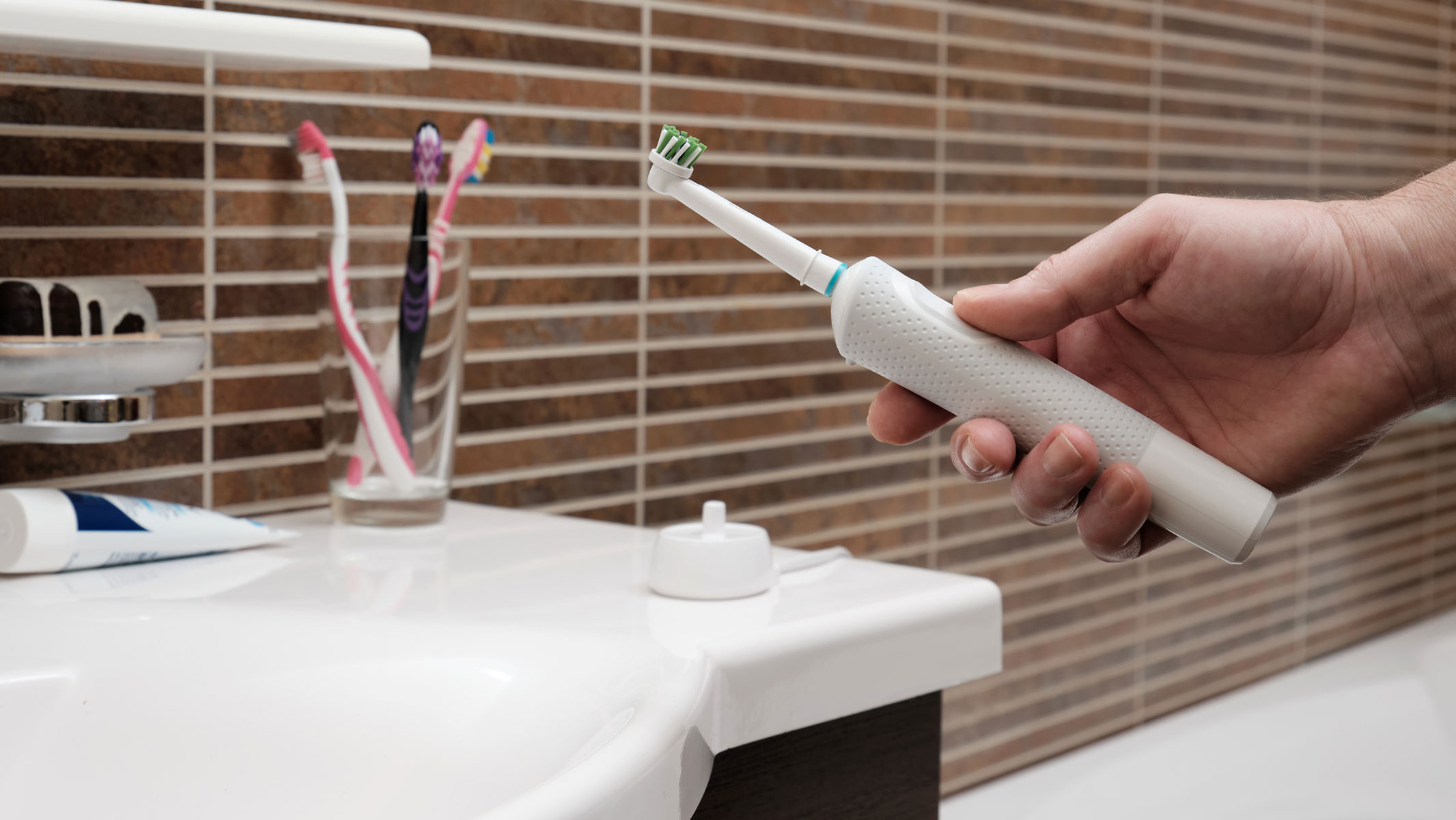 A close-up picture of a man holding an electric toothbrush near the bathroom sink