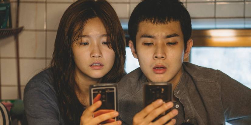 Park So-dam and Choi Woo-shik check their cellphones in a scene from Parasite.