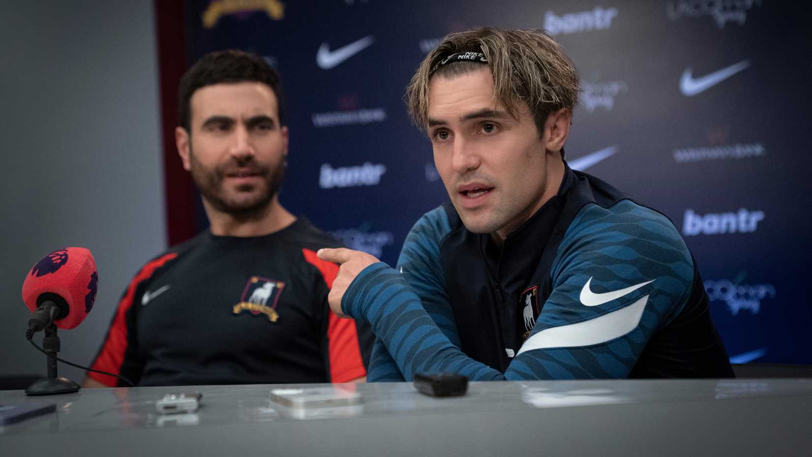 Phil Dunster's Jamie pointing towards Brett Goldstein's Roy during a press conference in Ted Lasso season 3