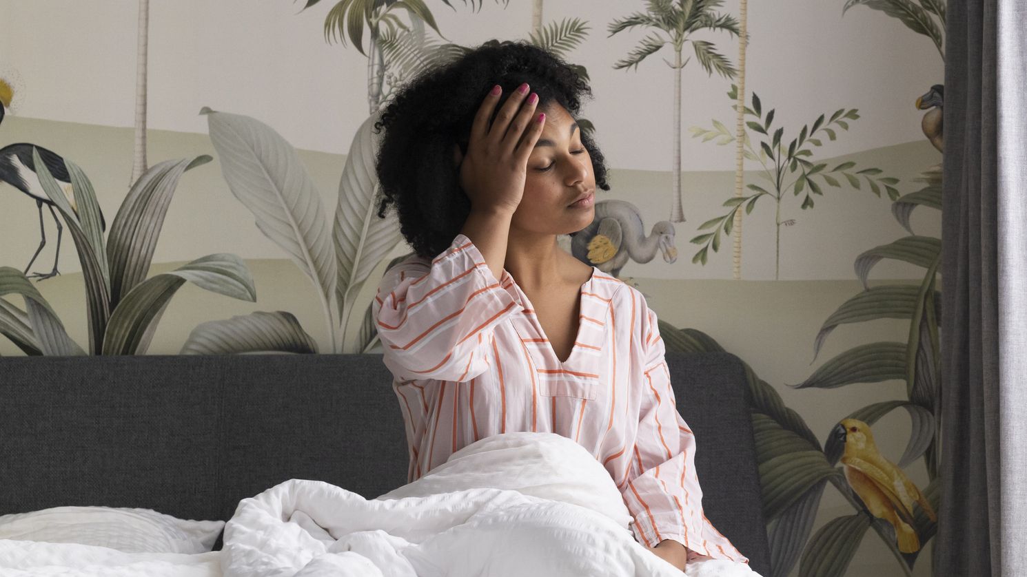 Woman sitting up in bed with her palm on her forehead and her eyes closed